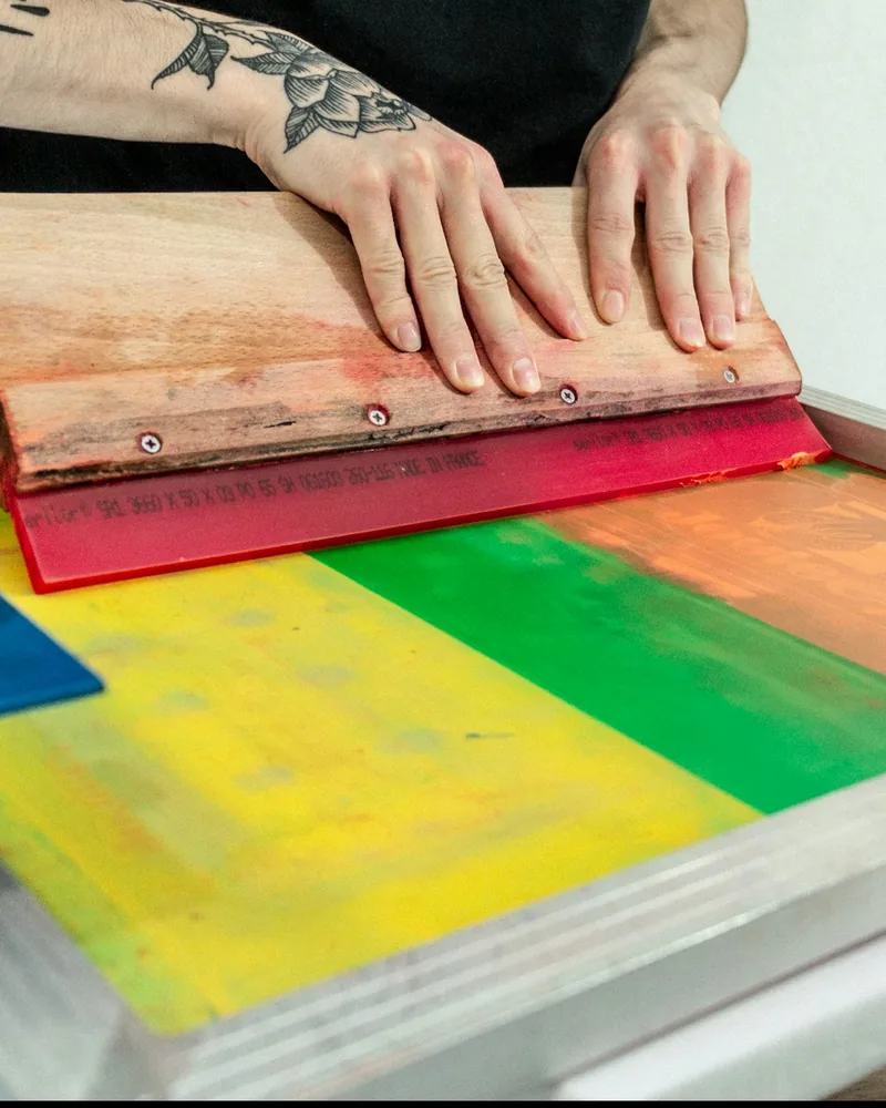 Racleta apoyada sobre una pantalla con tintas amarilla, verde, naranja y azul extendidas sobre la malla